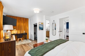 Een hotelkamer met een bed, een bureau, een stoel, een lamp, een spiegel en uitzicht op de gang.
