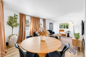 A modern living room with a round wooden dining table, black chairs, a sofa, a coffee table, and a potted plant. - South Bay Hideaway - 3BR/2BA Near LAX, Beaches & SoFi - Monthly Stays (Lawndale)