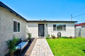 A residential house with a paved entrance, a front door, and a small garden area with a lawn and potted plants. - South Bay Hideaway - 3BR/2BA Near LAX, Beaches & SoFi - Monthly Stays (Lawndale)