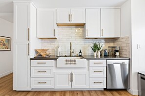 A modern kitchen with white cabinetry, a stainless steel dishwasher, and a brick backsplash. - South Bay Hideaway - 3BR/2BA Near LAX, Beaches & SoFi - Monthly Stays (Lawndale)