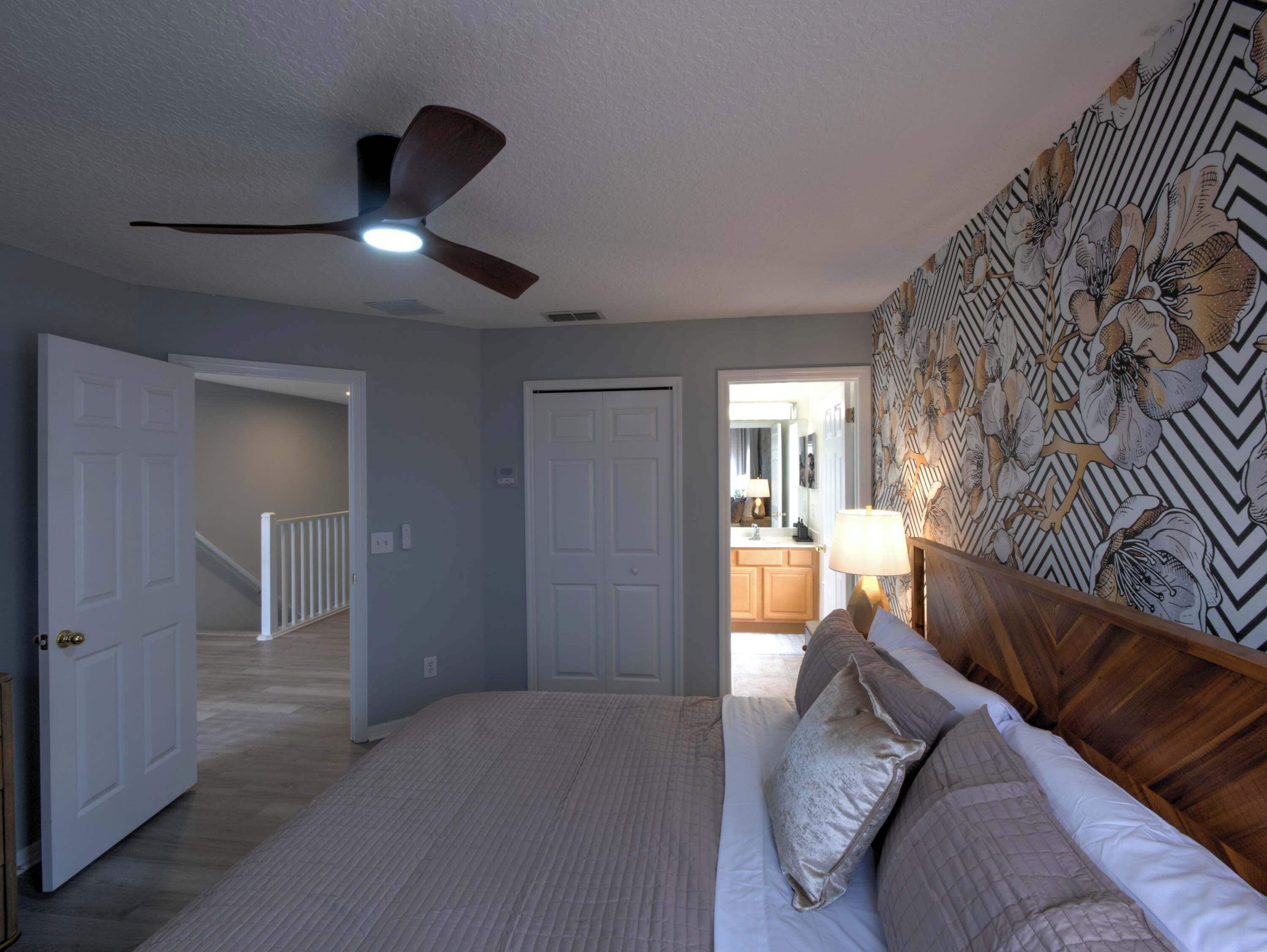 A bedroom with a bed, a ceiling fan, and a patterned wall.