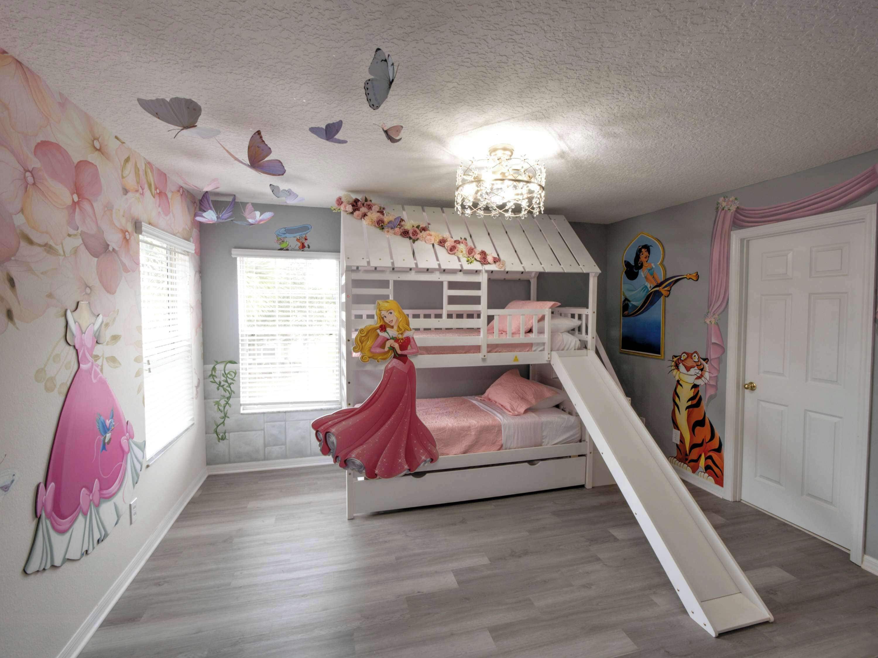 Une chambre d’enfant avec un lit superposé, un toboggan, des motifs floraux sur les murs et un plafond décoré d’autocollants représentant des papillons.