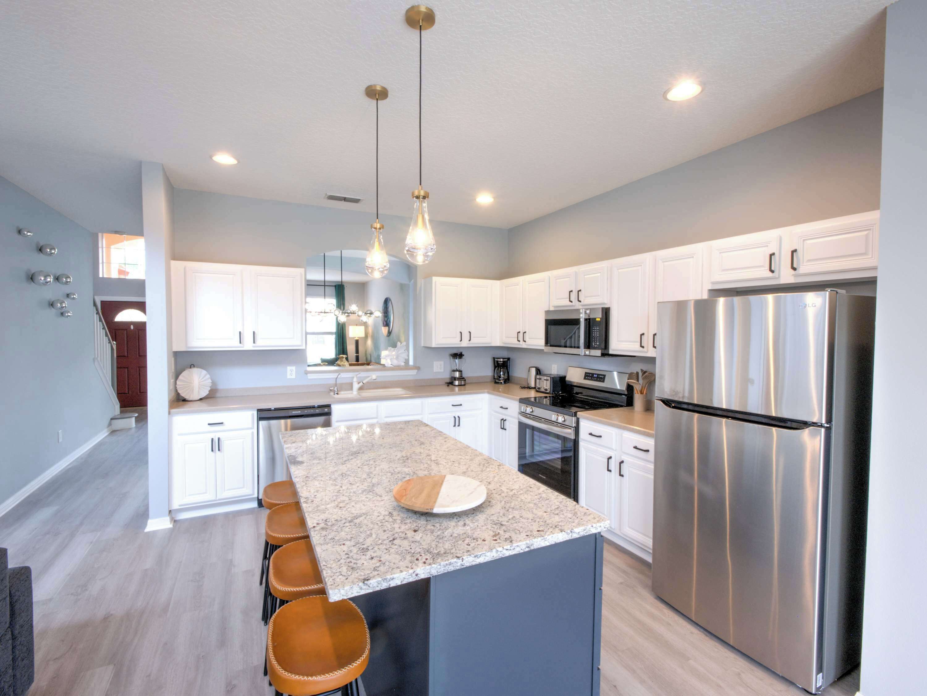 A modern kitchen with white cabinets, stainless steel appliances, and a granite island with bar stools.