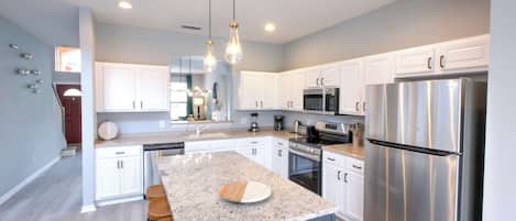 A modern kitchen with white cabinets, stainless steel appliances, and a granite island with bar stools.