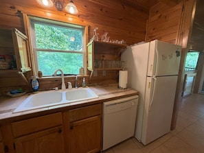 A kitchen with wooden cabinets, a white refrigerator, a sink, and a window with a view of greenery. - Mountain Lake Retreat | Kayaks, Dock + Fire Pit (Mentone)