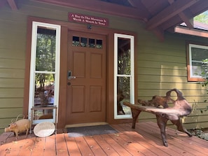 A wooden cabin with a brown door, a welcome sign, a metal sculpture, and a pig figurine on the porch. - Mountain Lake Retreat | Kayaks, Dock + Fire Pit (Mentone)