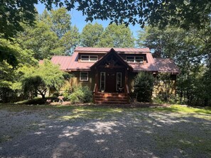 A two-story house with a red roof, a front porch, and a gravel driveway.