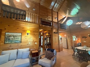 A wooden interior with a sofa, armchair, dining table, and kitchen area. - Mountain Lake Retreat | Kayaks, Dock + Fire Pit (Mentone)