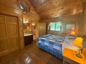 A wooden cabin bedroom with a bed, dresser, and a window with curtains.