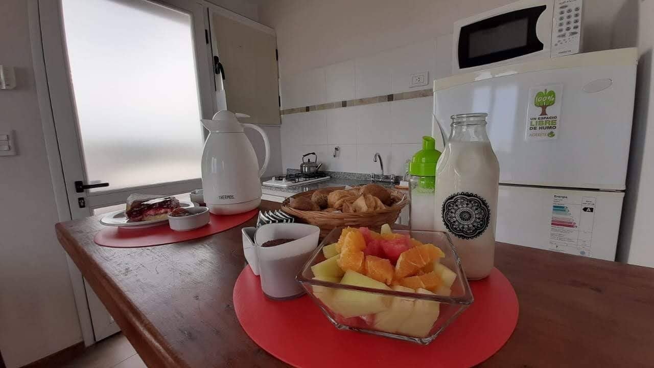 Una cocina con microondas, refrigerador, cafetera y frutero sobre la encimera.