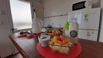 Una cocina con microondas, refrigerador, cafetera y frutero sobre la encimera.