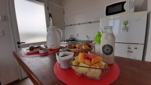 A kitchen with a microwave, a refrigerator, a coffee maker, and a fruit bowl on the counter.
