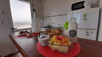 Una cocina con microondas, refrigerador, cafetera y frutero sobre la encimera.