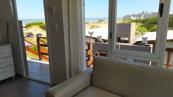 Una habitación con vista al mar, un sofá, una silla de madera y un comedor con mesa y sillas.