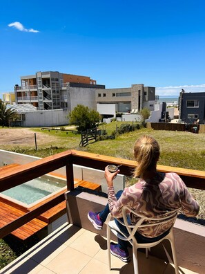 Une personne est assise sur une chaise, face à une piscine, avec vue sur des bâtiments modernes et un ciel dégagé.