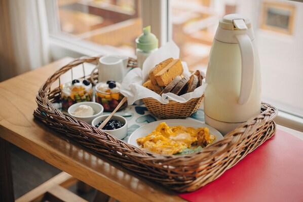 Un plateau de petit-déjeuner avec des œufs, des toasts, des fruits et du café, posé sur une table en bois près d’une fenêtre.