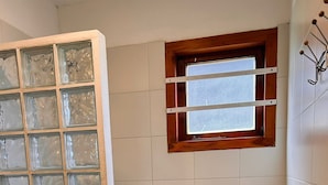 Casa de banho com banheira, cabine de duche em vidro, janela e parede revestida a azulejos.