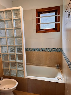 Un baño con bañera, cabina de ducha de vidrio, ventana y pared con azulejos.