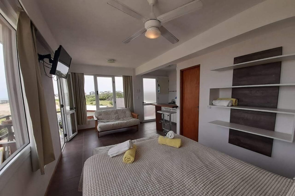 Una habitación de hotel con una cama, un televisor montado en la pared, un ventilador de techo y vistas al exterior.
