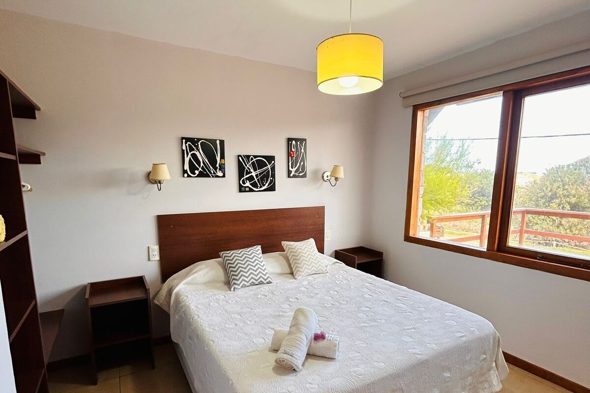 Una habitación de hotel con una cama grande, una mesita de noche, una ventana con vistas y una obra de arte en la pared.