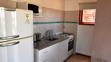 Una cocina compacta con refrigerador, estufa, lavamanos y armarios.