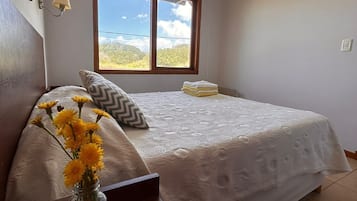 Un dormitorio con cama, una ventana con vistas, un florero con flores y una lámpara.