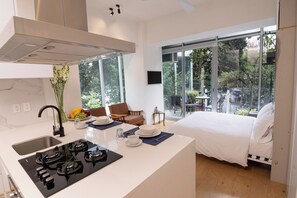 A modern hotel room with a kitchen area, a dining space, and a large window offering a view of the outdoors. - Mini Loft w/ Cibeles Fountain View - Balcony & AC (Ciudad de México)