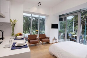 A modern hotel room with a large bed, a dining area with chairs, a kitchen area, and a large window offering a view of the outdoors. - Mini Loft w/ Cibeles Fountain View - Balcony & AC (Ciudad de México)