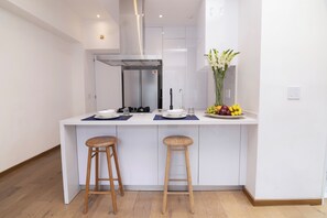 A modern kitchen with white cabinetry, a stainless steel range hood, a built-in sink, and two wooden stools. - Mini Loft w/ Cibeles Fountain View - Balcony & AC (Ciudad de México)