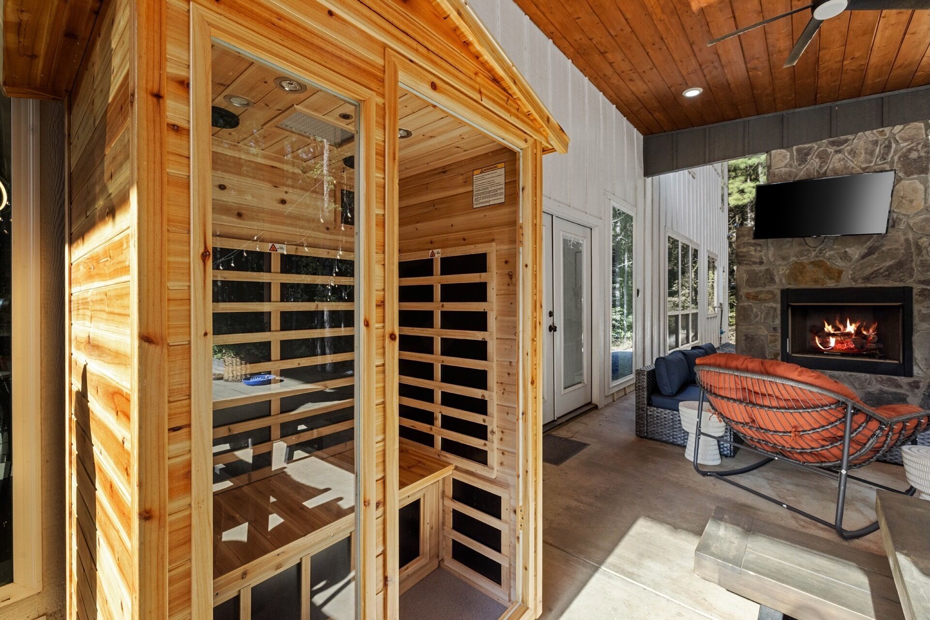 Un sauna aux murs en bois et à la porte en verre, une cheminée en pierre et un coin salon avec un fauteuil suspendu.