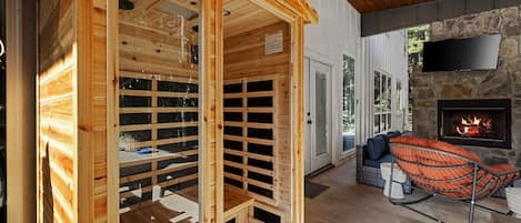 A sauna with wooden walls and a glass door, a stone fireplace, and a seating area with a swing chair.