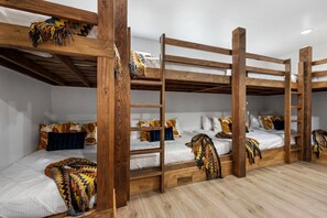 Ein Schlafraum mit Etagenbetten, Holzrahmen, weißer Bettwäsche und bunten Decken.