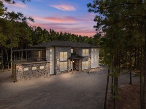 A two-story stone house with a balcony, surrounded by a forest. - Group Retreat | Hot Tub + Sauna | Sleeps 24 (Broken Bow)