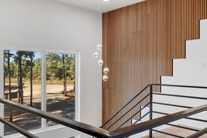 Een modern interieur met een wand van houten lambrisering, een trap met metalen leuningen en uitzicht op een bos door een glazen deur.