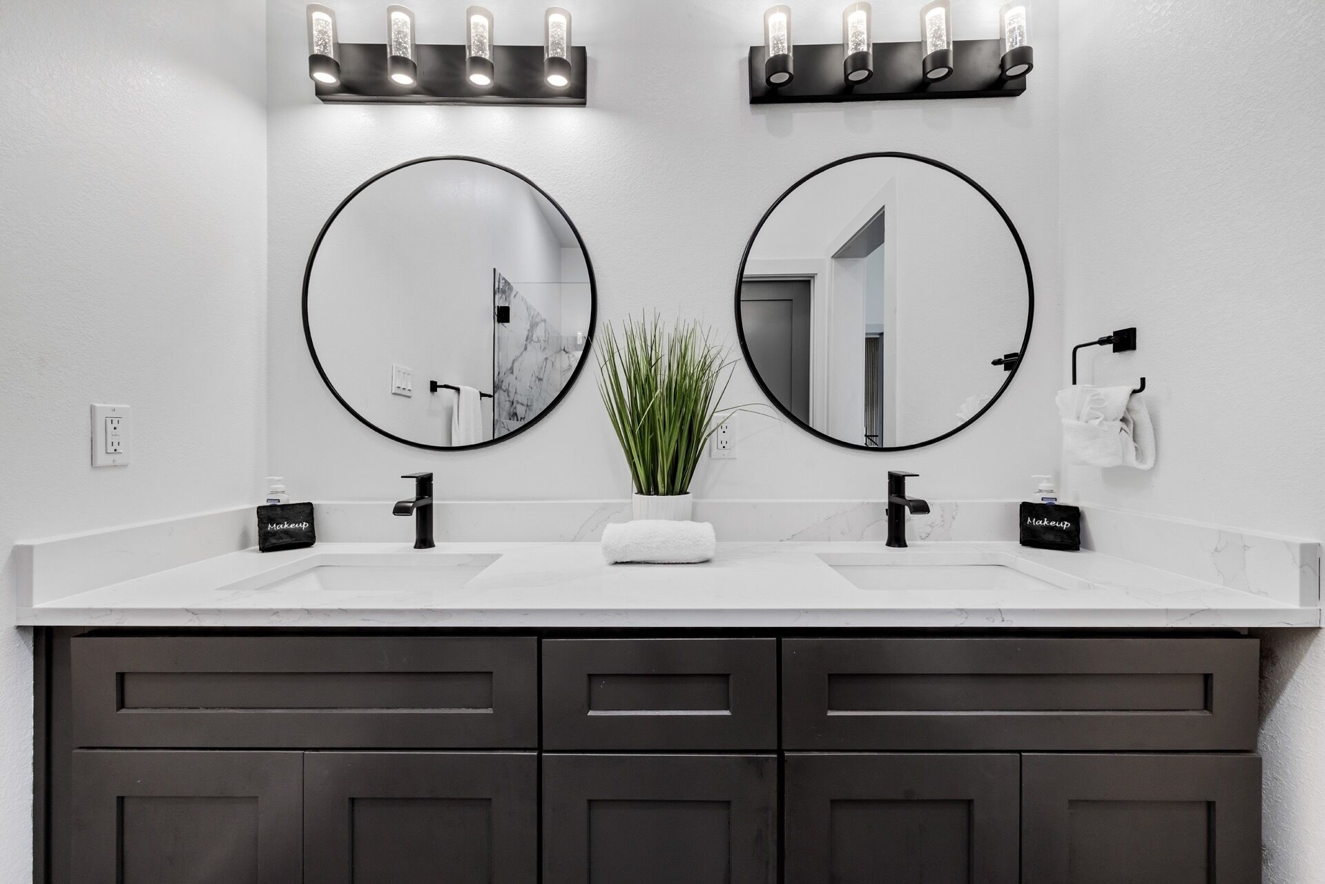 A bathroom with two round mirrors, a white countertop, a potted plant, and a towel rack.