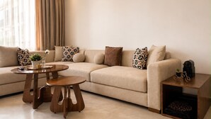 Ein modernes Wohnzimmer mit einem beigefarbenen Sofa, gemusterten Kissen, einem Holztisch und einem kleinen Beistelltisch mit einer Pflanze.
