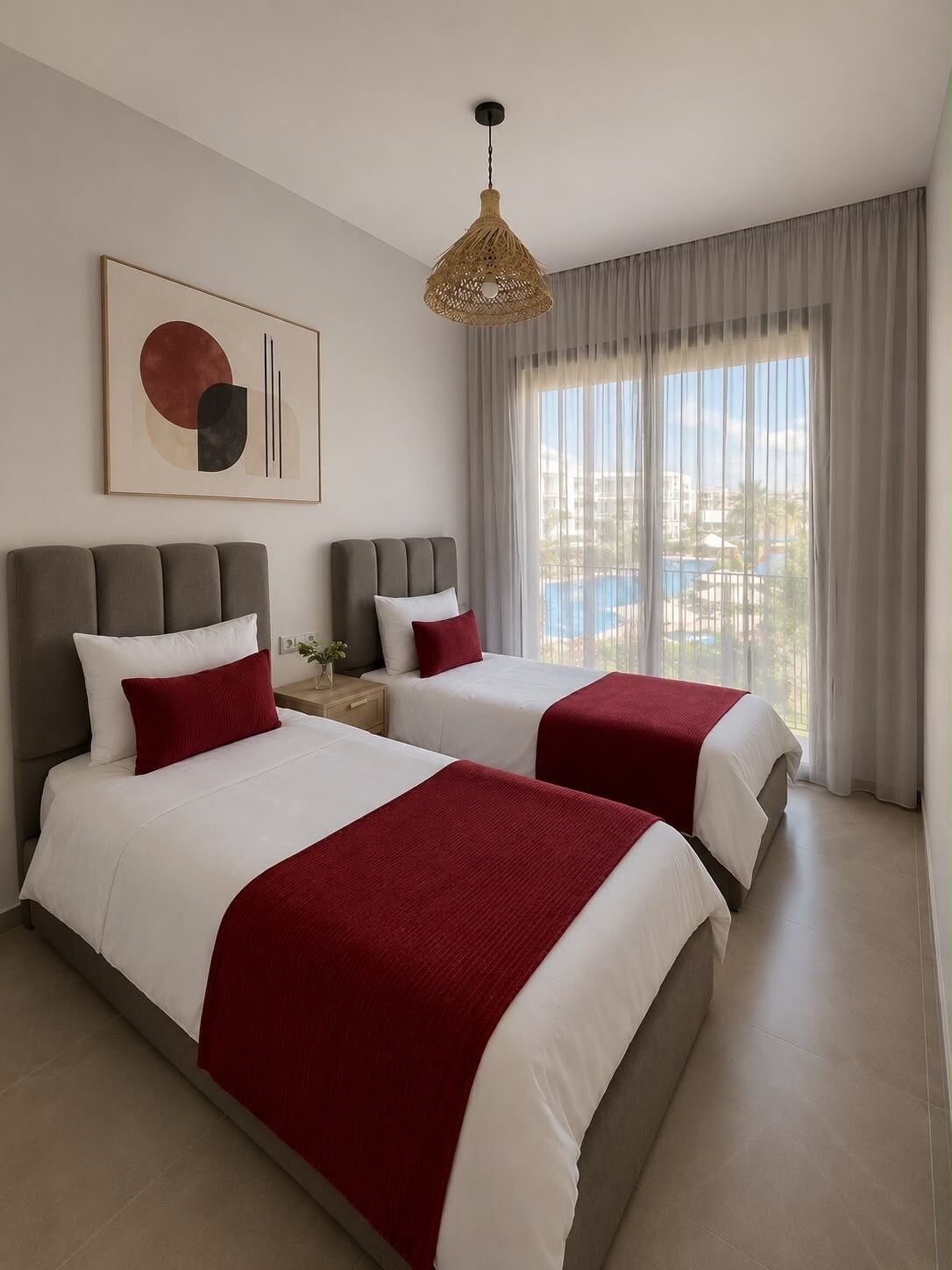 Une chambre d’hôtel avec deux lits, une grande fenêtre avec des rideaux, un luminaire suspendu et un tableau abstrait accroché au mur.