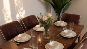 Ein Esstisch mit weißen Tellern, Schüsseln und Gläsern, umgeben von braunen Polstermöbelstühlen.