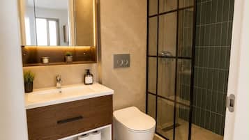 Une salle de bain moderne avec une douche à parois de verre, des toilettes blanches et un meuble-lavabo avec un miroir et un évier.