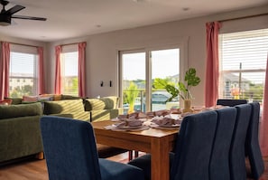 A living room with a sofa, chairs, a dining table set for two, and a view of a body of water through large windows. - Vilano Beach | Private Pool + Pickleball + Hot Tub (St Augustine)
