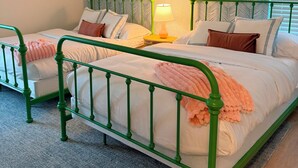 Ein Schlafzimmer mit zwei Betten aus grünem Metall, weißer Bettwäsche und einem gemusterten Wandpapier.