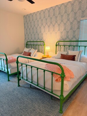 Un dormitorio con dos camas de metal verde, ropa de cama blanca y un papel tapiz estampado.