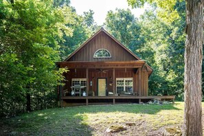 Une cabane en bois dotée d’un porche, de grandes fenêtres et d’une terrasse couverte.