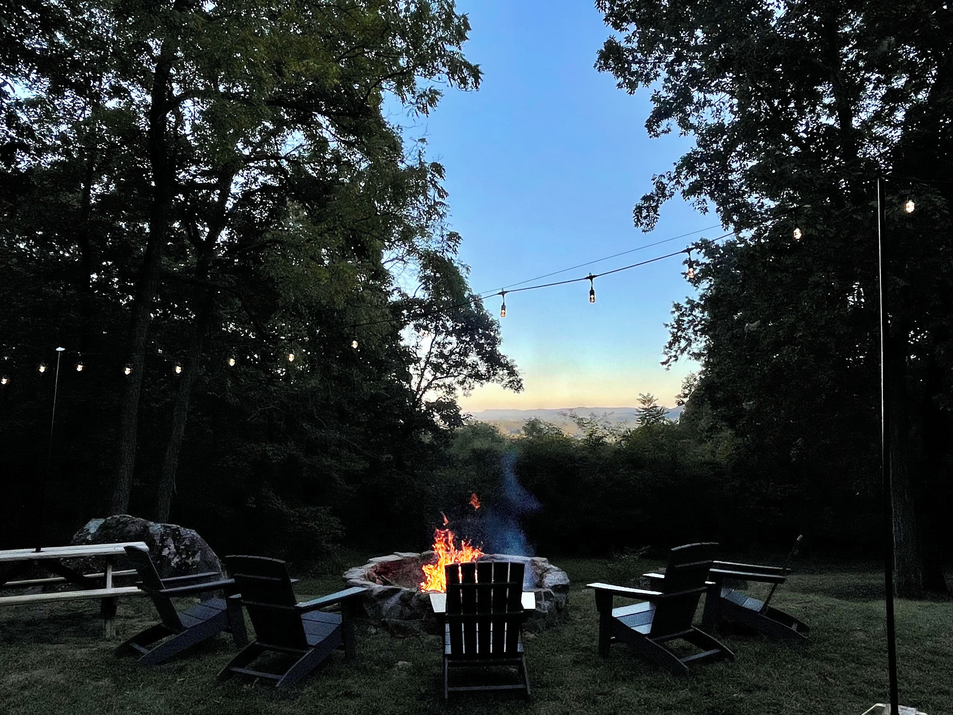 Un espace extérieur aménagé avec des chaises et un foyer, entouré d  ’arbres et offrant une vue sur un ciel dégagé.
