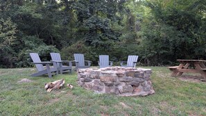 A stone fire pit surrounded by Adirondack chairs and a picnic table in a grassy area with dense trees in the background. - Buffalo Valley Retreat-Secluded 2-bedroom cabin 8 minutes from Jasper (Jasper)