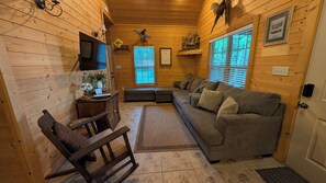 L’intérieur chaleureux d’un chalet, avec un revêtement mural en bois, un canapé, un fauteuil, un bureau et un téléviseur.