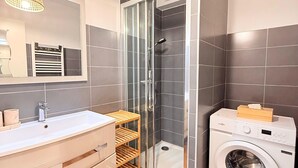 Un baño moderno con ducha envuelta en vidrio, lavadora integrada y tocador con espejo.