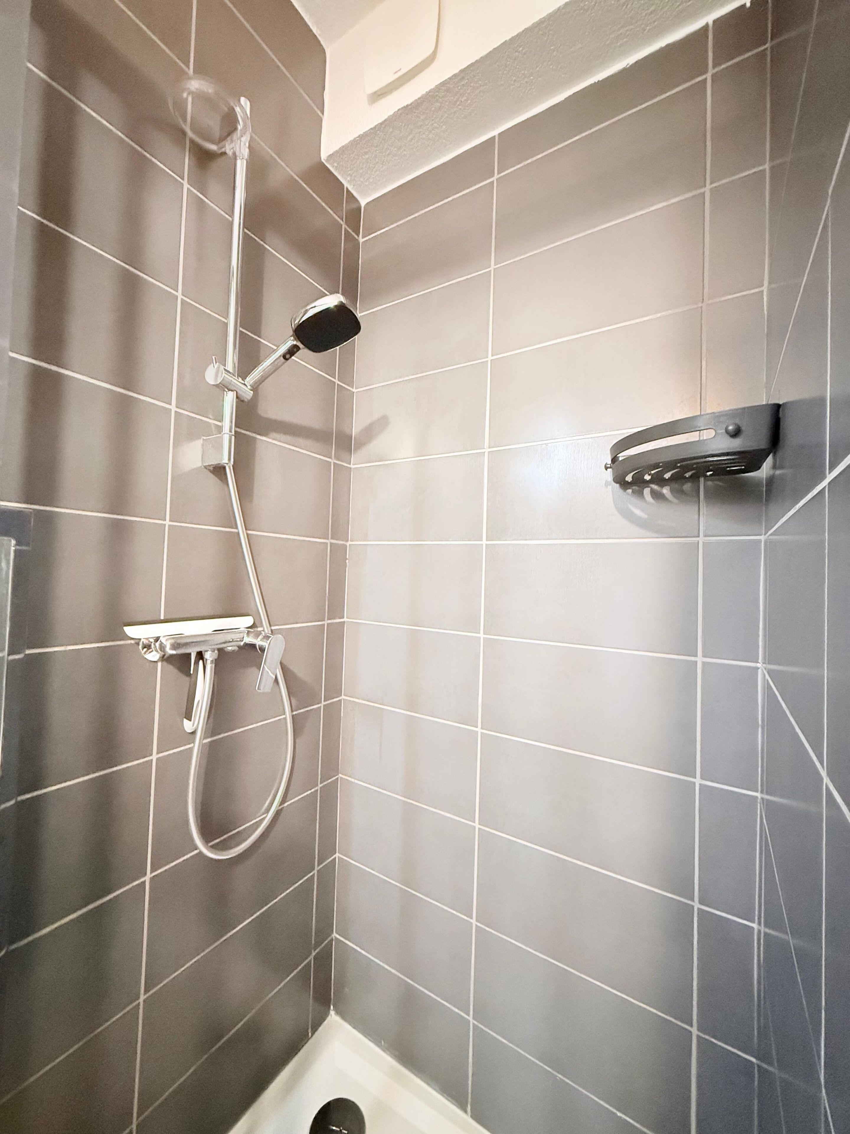 A shower with a handheld showerhead and a wall-mounted faucet in a tiled bathroom.