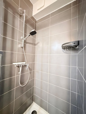 Una ducha con cabezal de ducha de mano y grifo empotrado en un baño con azulejos.