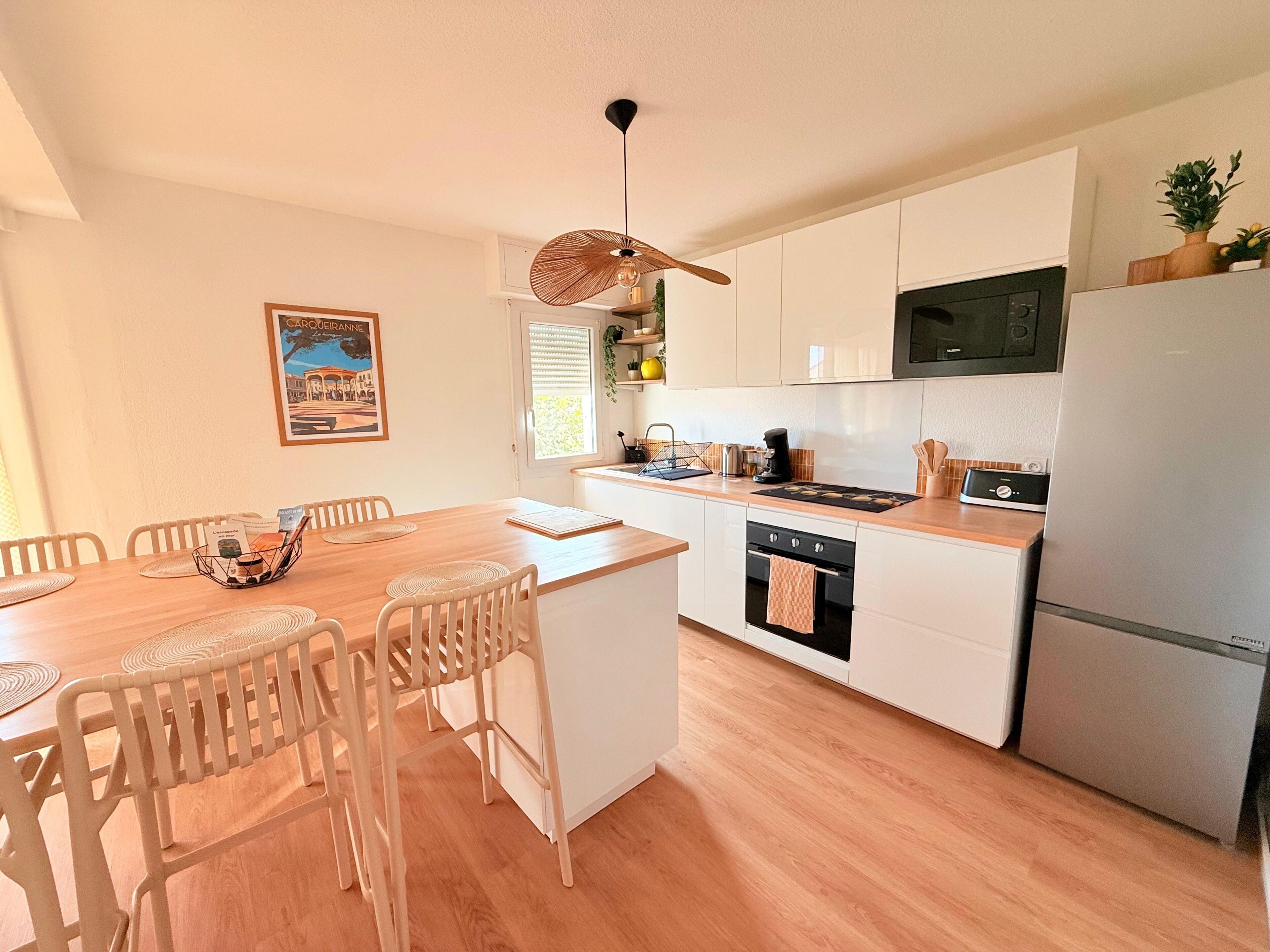A modern kitchen with white cabinets, a stainless steel refrigerator, a microwave, and a wooden dining table with chairs.